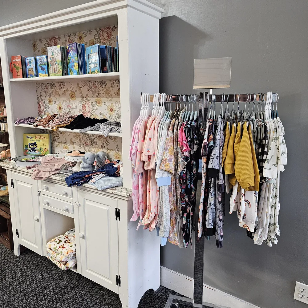 Colorful children's clothing beside shelves of books and soft toys